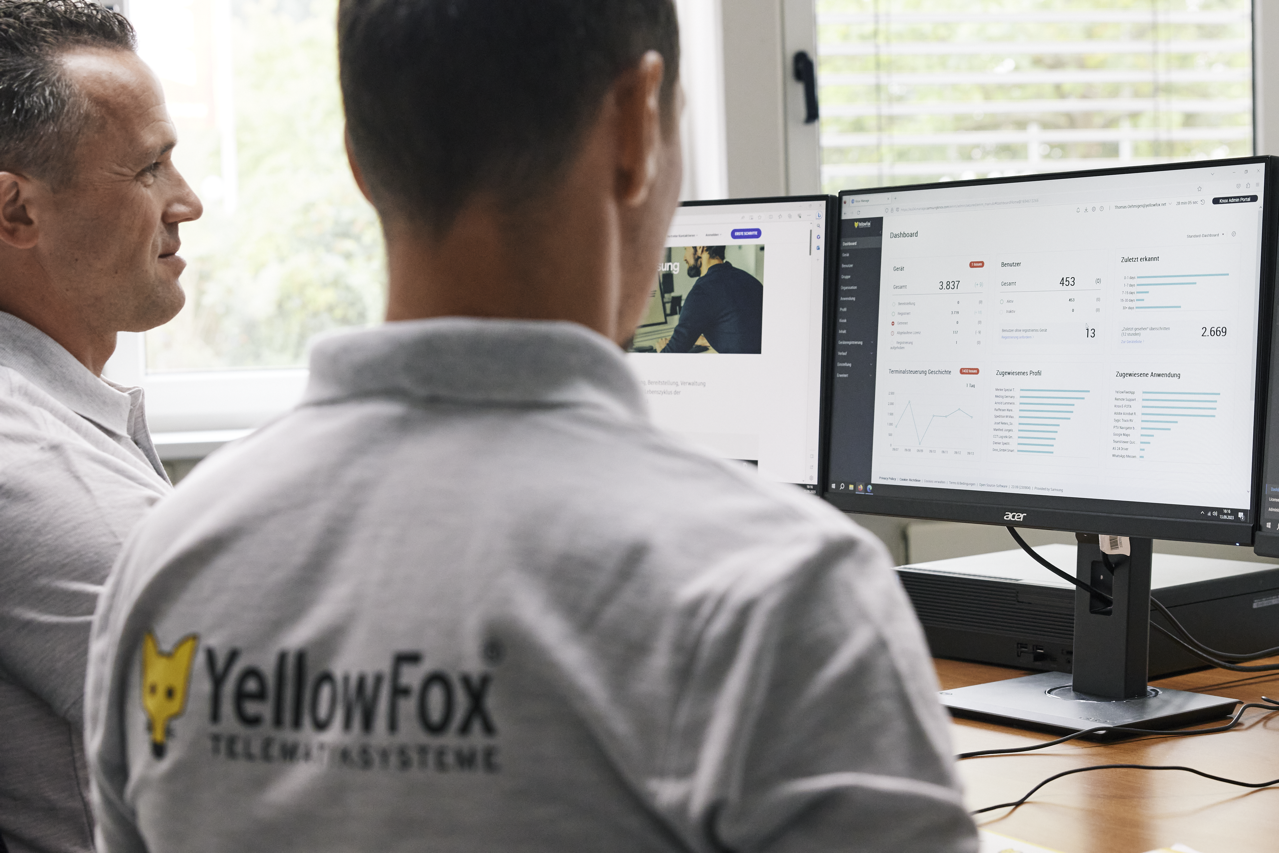 Two YellowFox employees sitting in front of a double-monitor set-up to view their Knox Admin Portal dashboard.